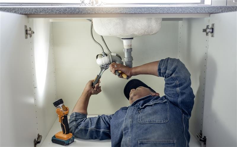 Plumber repairing pipes beneath a bathroom sink in San Fernando